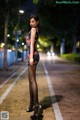 A woman in a black dress standing on a sidewalk at night.