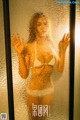 A woman in a white bikini standing in front of a glass door.