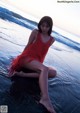 A woman in a red dress sitting on the beach.