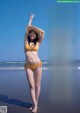 A woman in a yellow bikini standing on a beach.