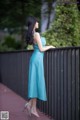 A woman in a blue dress leaning against a fence.