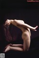 A naked woman is sitting on a black surface.