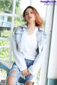 A woman sitting on a window sill wearing ripped jeans and a denim jacket.