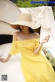 A woman in a yellow dress and straw hat sitting on a bed.