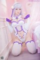 A woman in a white and purple outfit sitting on a bed.