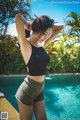 A woman in a black top and gray shorts by a pool.