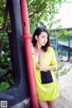 A woman in a yellow dress leaning against a red pole.