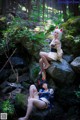 A couple of women sitting on top of a rock in the woods.